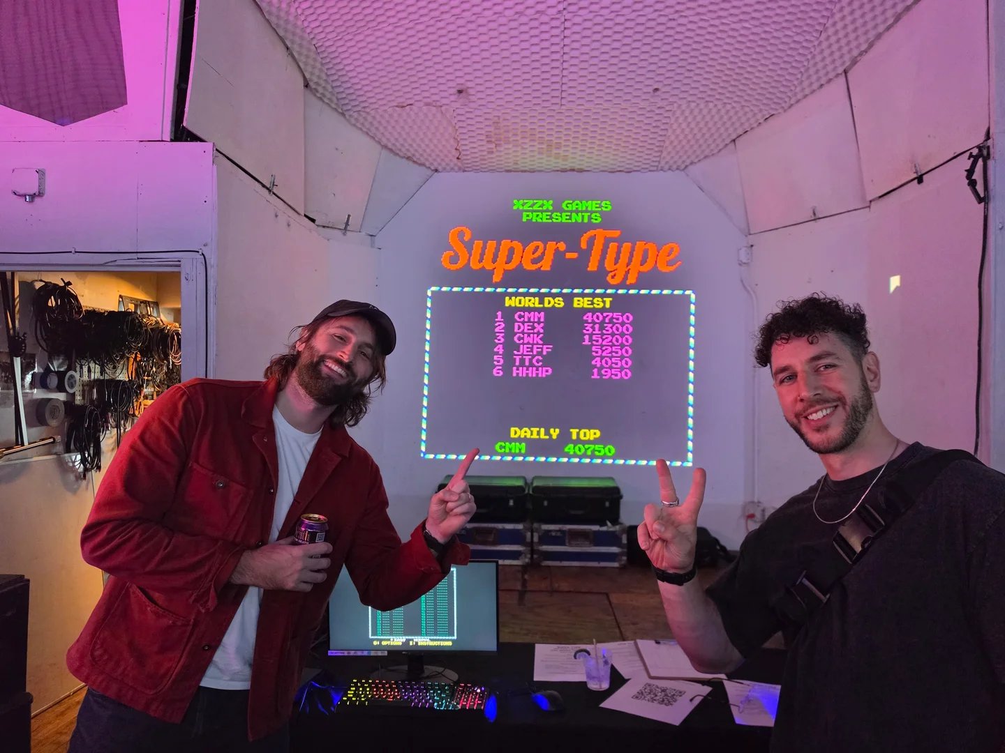 Two people beside the projected SUPER-TYPE leaderboard after the competition.